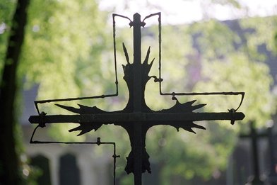 Schwarzes, verwittertes Kreuz von grünem Hintergrund - Copyright:  Foto: epd bild/Neetz
